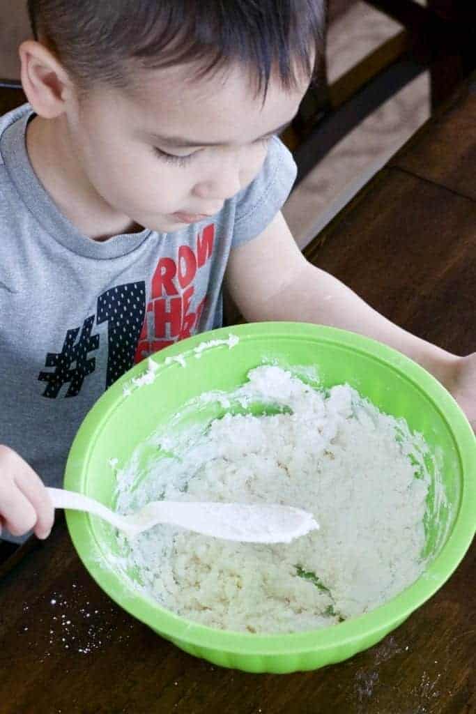 Mixing up homemade playdough in a bowl. This is a great toddler activity they can help with!