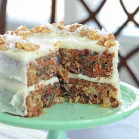 A whole carrot cake with two slices taken out of it on a green cake plate