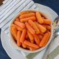 A bowl of baby carrots on a striped napkin and blue placemat surrounded with flowers