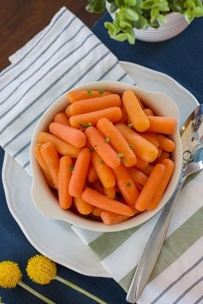 A bowl of baby carrots on a striped napkin and blue placemat surrounded with flowers