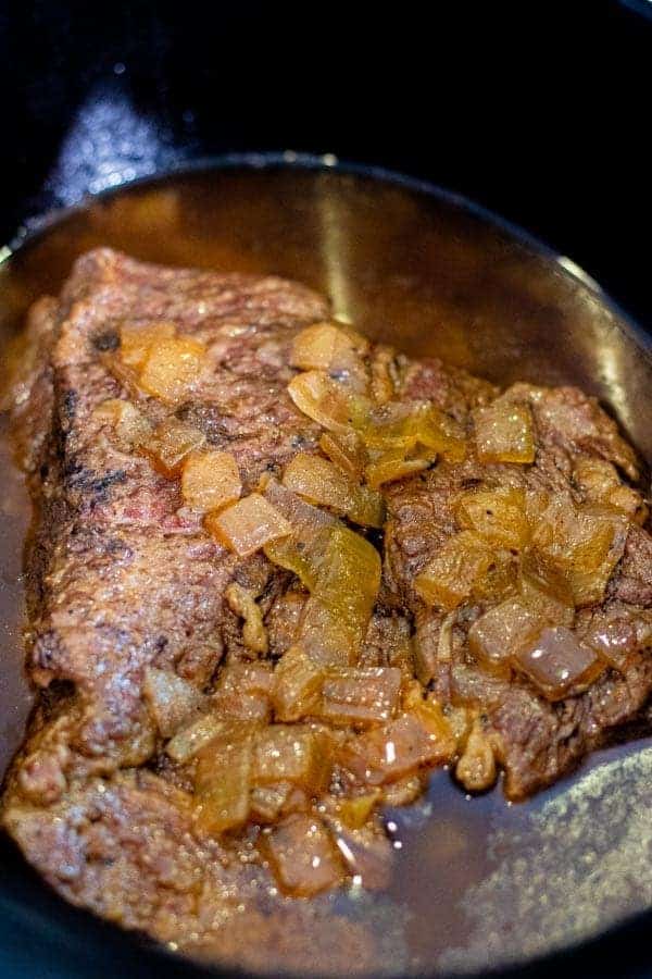 chuck roast pot roast in the crock pot with onions on top