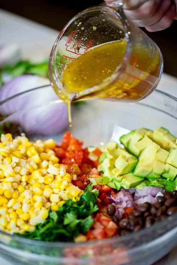 pouring vinaigrette on top of corn salad