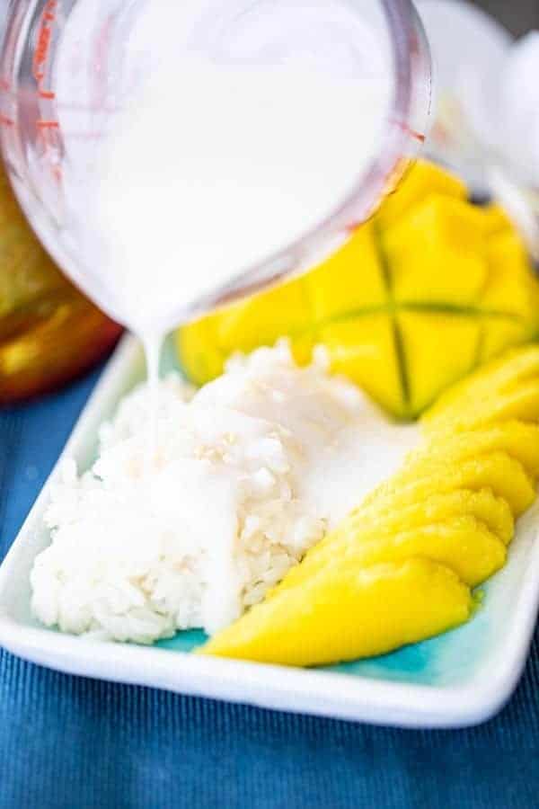 coconut sauce being poured on top of mango sticky rice