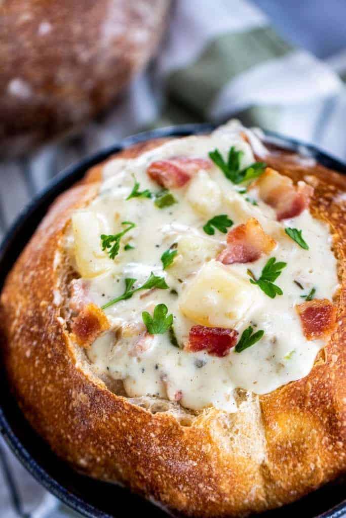 A closeup of a bread bowl with clam chowder topped with bacon and fresh parlsey.