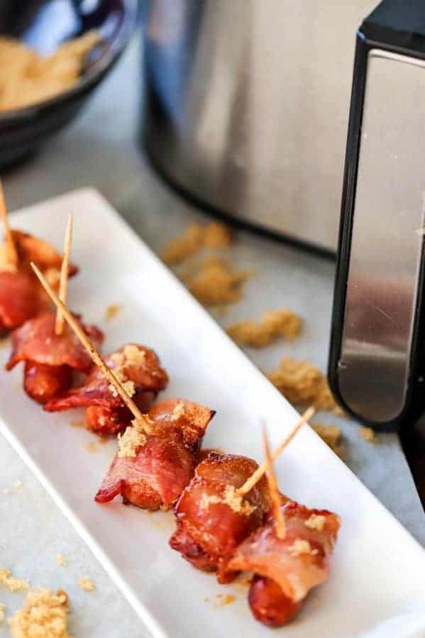 bacon wrapped smokies with brown sugar on a white tray with an air fryer handle in the background