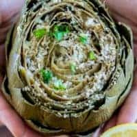 two hands holding a stuffed artichoke