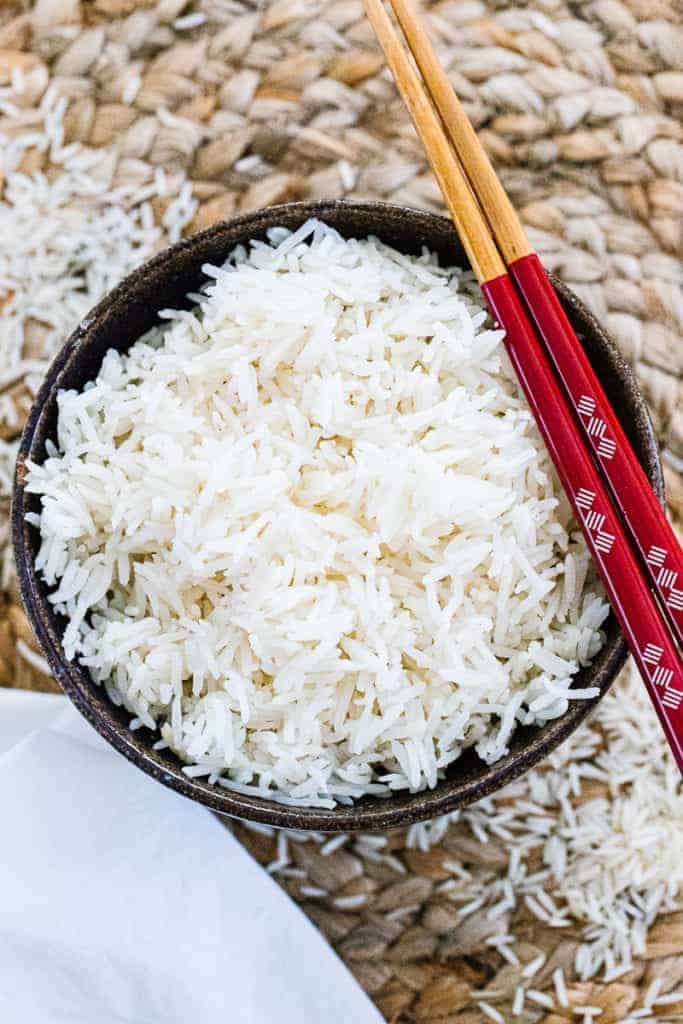 a bowl of basmati rice with red chopsticks and a white napkin