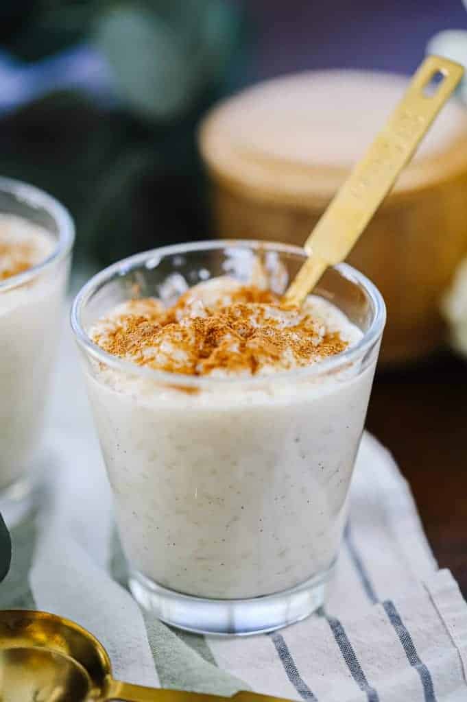 a closeup of a cup of vanilla rice pudding with cinnamon and a gold spoon