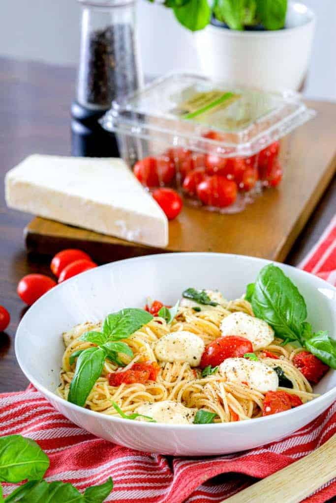 margherita pasta with tomatoes, cheese, and pepper grinder in the background