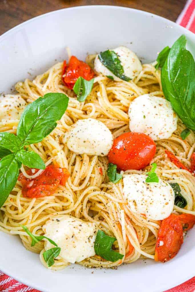 a bowl of angel hair pasta with basil, tomatoes, and mozzarella