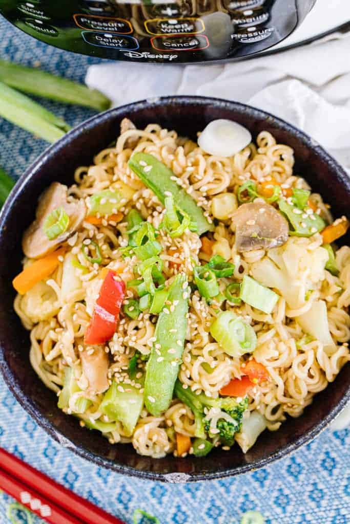 Top view of ramen stir fry surrounded by chopsticks, green onions, white cloth, and instant pot