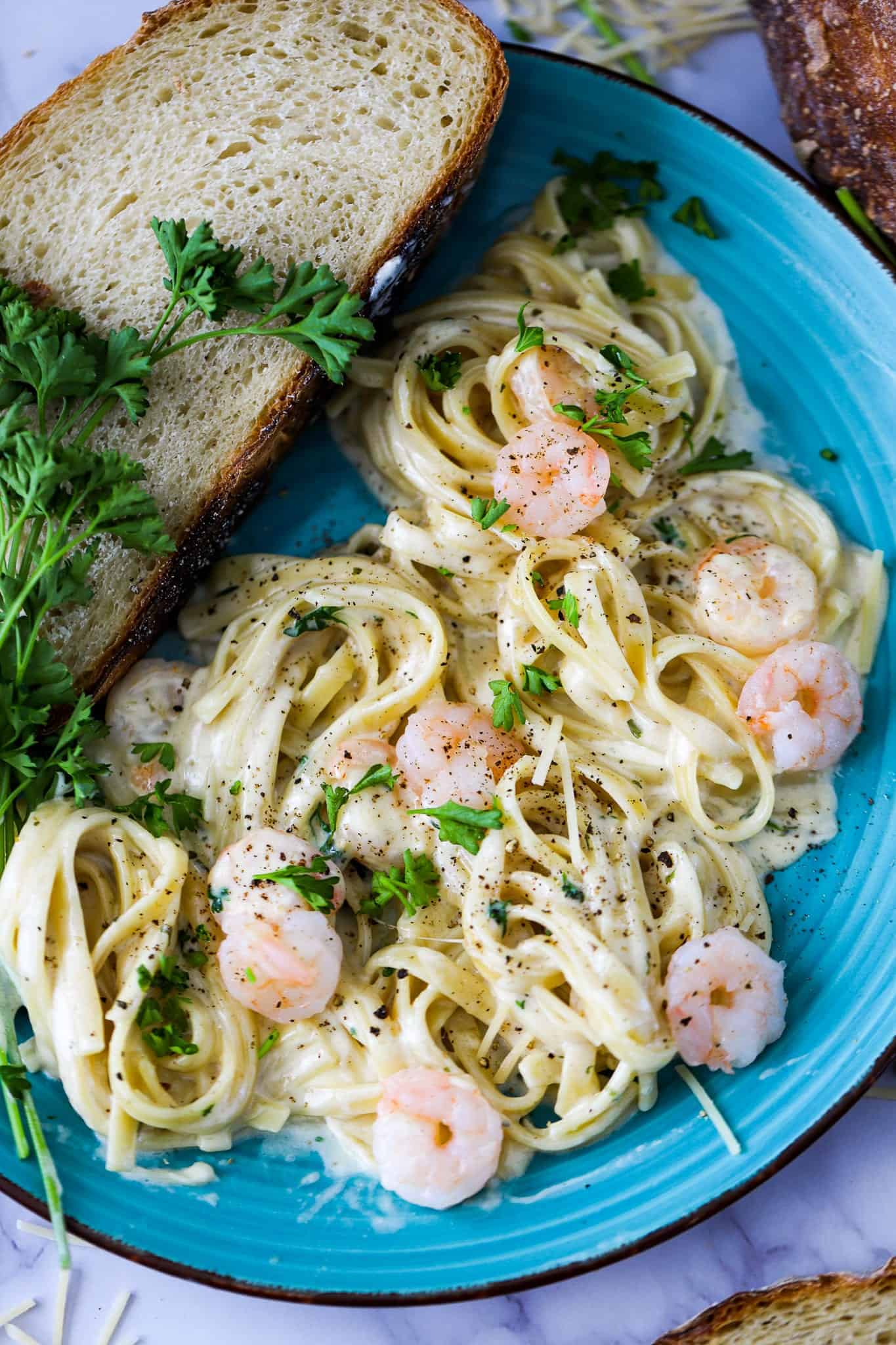 a plate of shrimp alfredo with bread on a blue plate