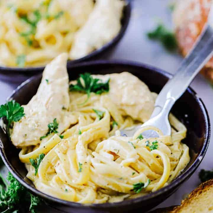 Chicken Alfredo garnished with parsley in a dark bowl with a fork and spoon in bowl