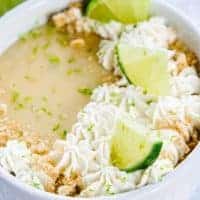 Close up of key lime pie topped with cream, limes, and graham cracker crumbs