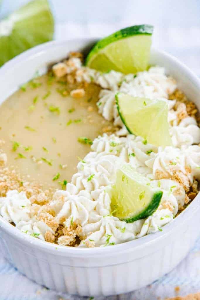 Close up of key lime pie topped with cream, limes, and graham cracker crumbs