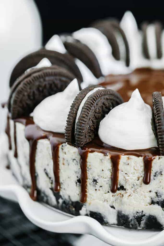 Close up of whole oreo cheesecake with chocolate drizzle, oreo, and cream topping