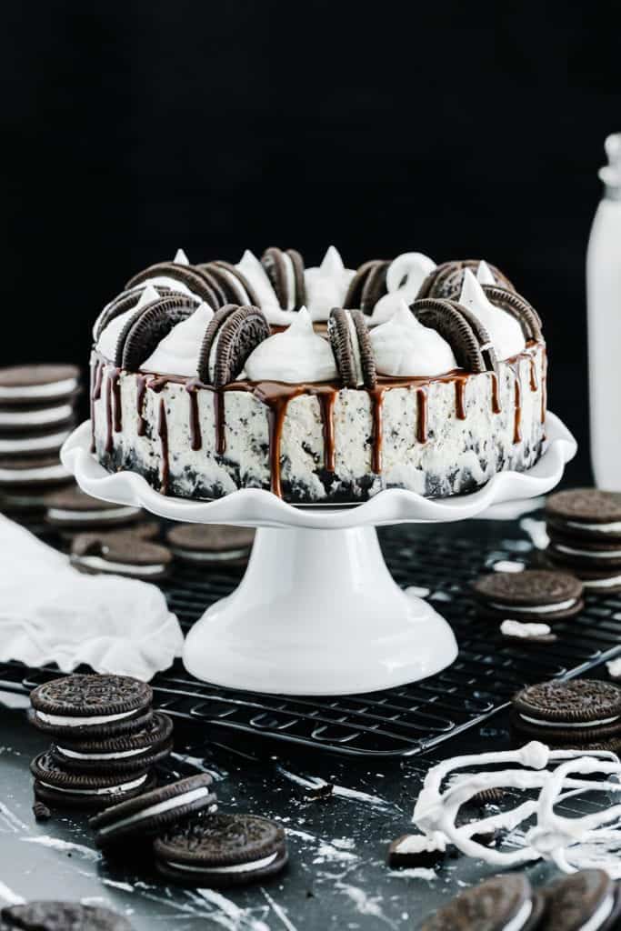 Oreo cheesecake topped with chocolate drizzle, whole oreos, and cream surrounded by oreos and glass of milk