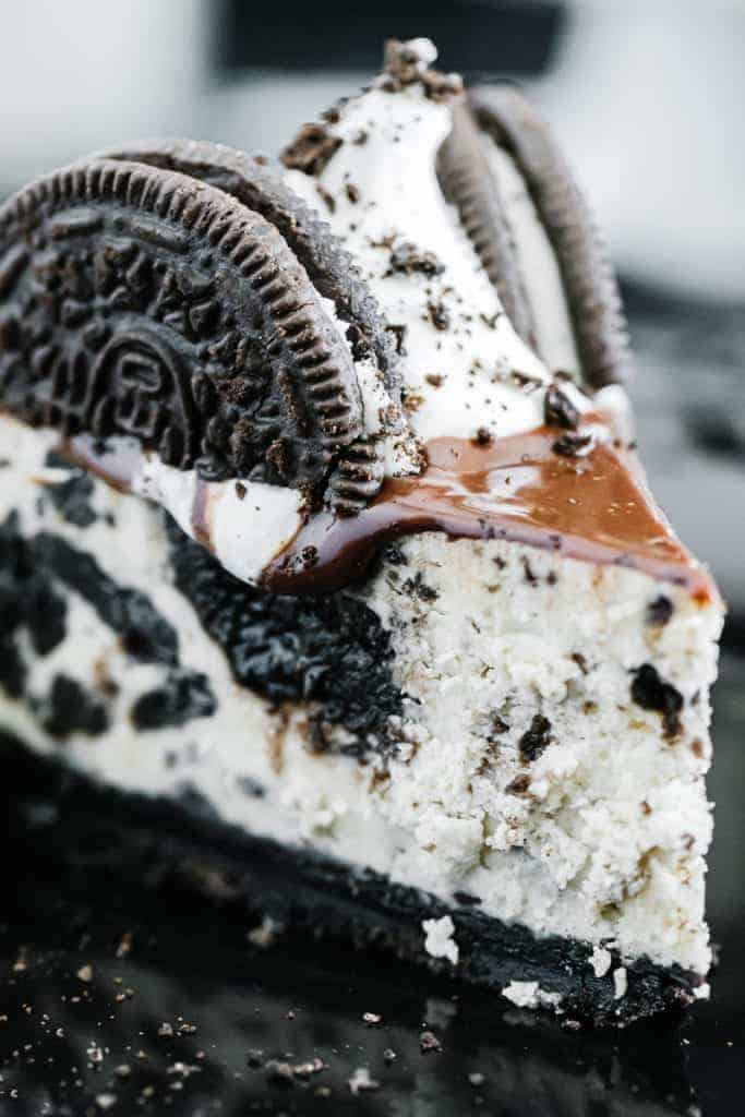 Close up slice of oreo cheesecake topped with chocolate drizzle, oreos, and cream