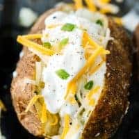 Close up of single baked potato topped with cheese, sour cream, and scallions