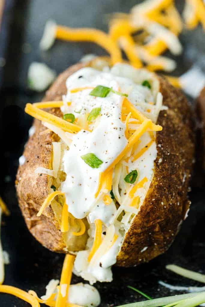 Close up of single baked potato topped with cheese, sour cream, and scallions