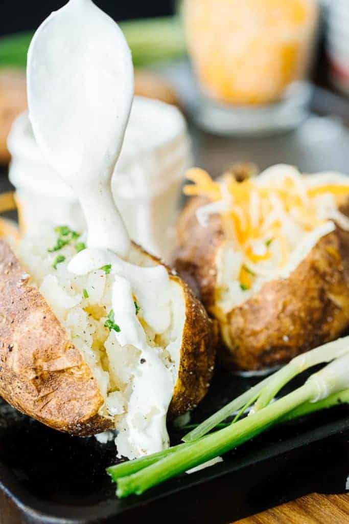 Baked potato with spoon of sour cream being drizzled over