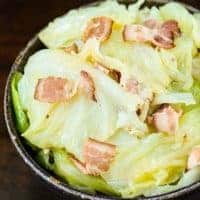 top view of cooked cabbage and bacon pieces on dark bowl