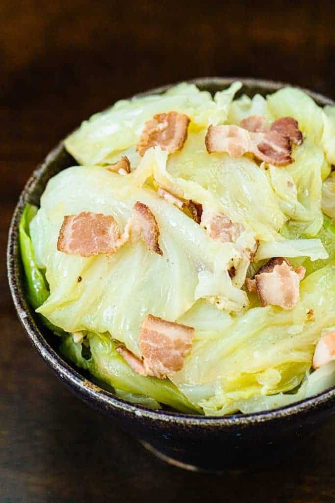 top view of cooked cabbage and bacon pieces on dark bowl