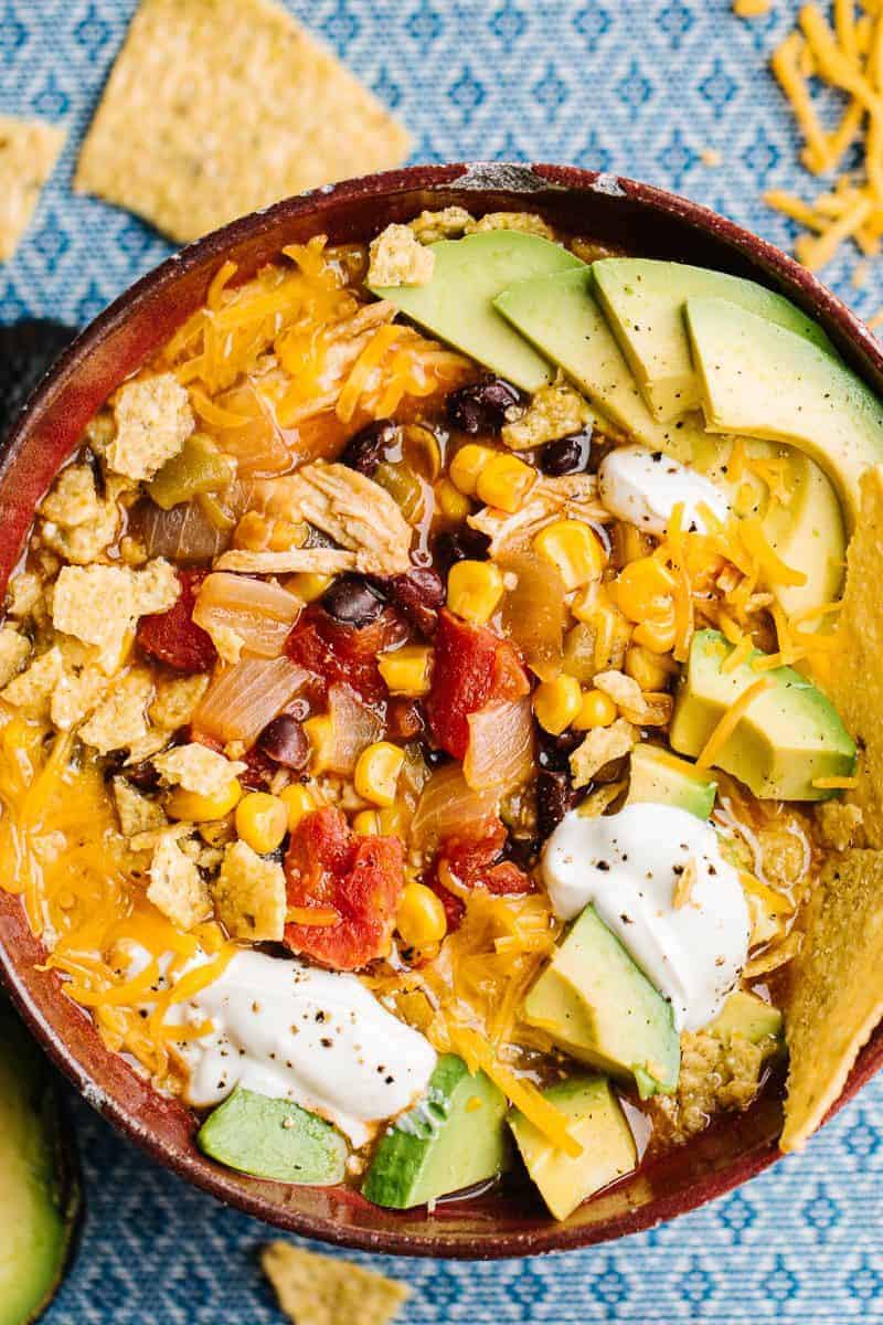 top view of enchilada soup topped with avocado, sour cream, and tortilla chips placed on a blue tablecloth