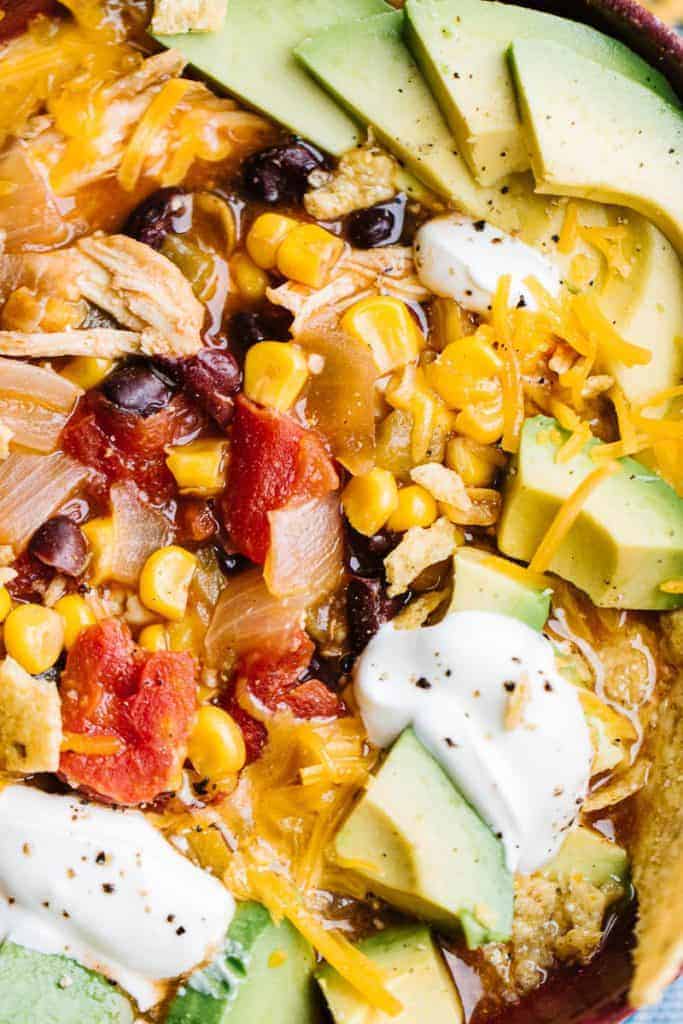 close up of enchilada soup topped with cheese, sour cream, and avocados