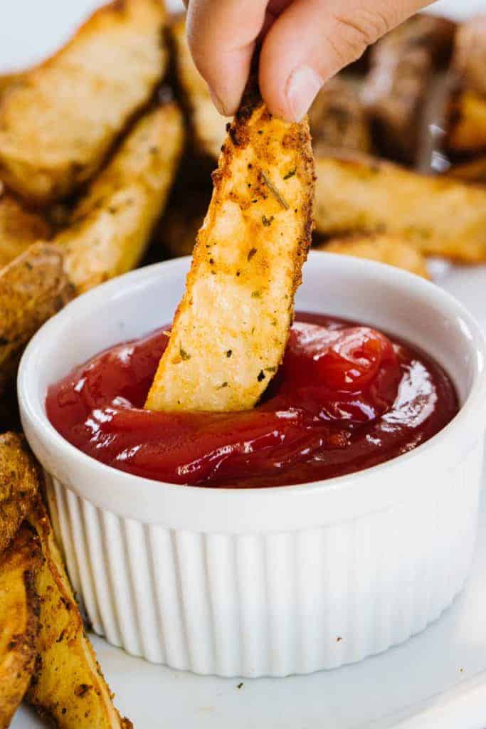 Air fried potato wedge being dipped in ketchup