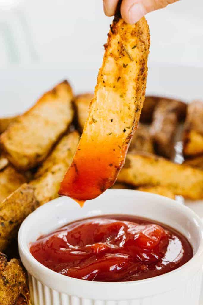  air fried potato wedge being pulled out of ketchup