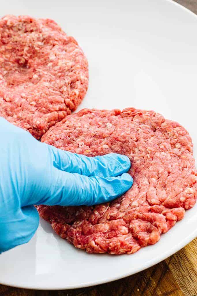 Gloved finger pressing into raw hamburger patty