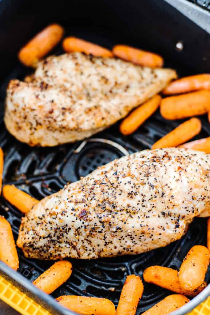Air fryer chicken breasts in air fryer topped with seasoning and next to carrots