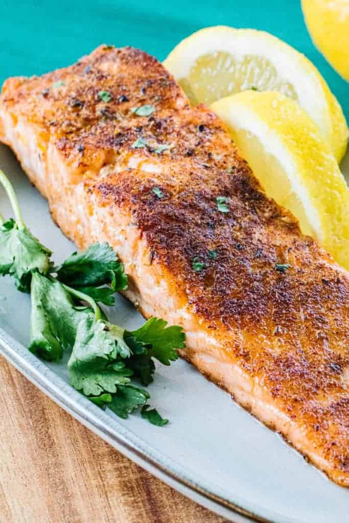 Air fried salmon topped with parsley on a white plate next to lemon wedges and parsley next to a teal cloth