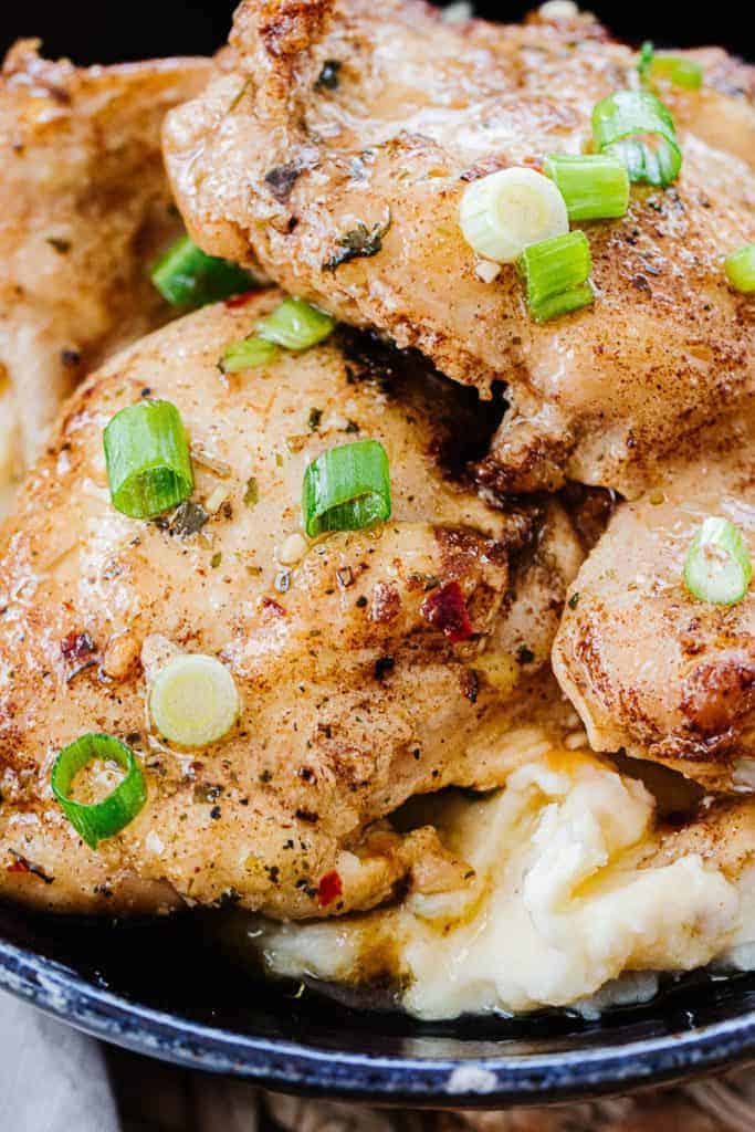 Close up of Instant Pot chicken thighs made from frozen in dark bowl on mashed potatoes and topped with green onions