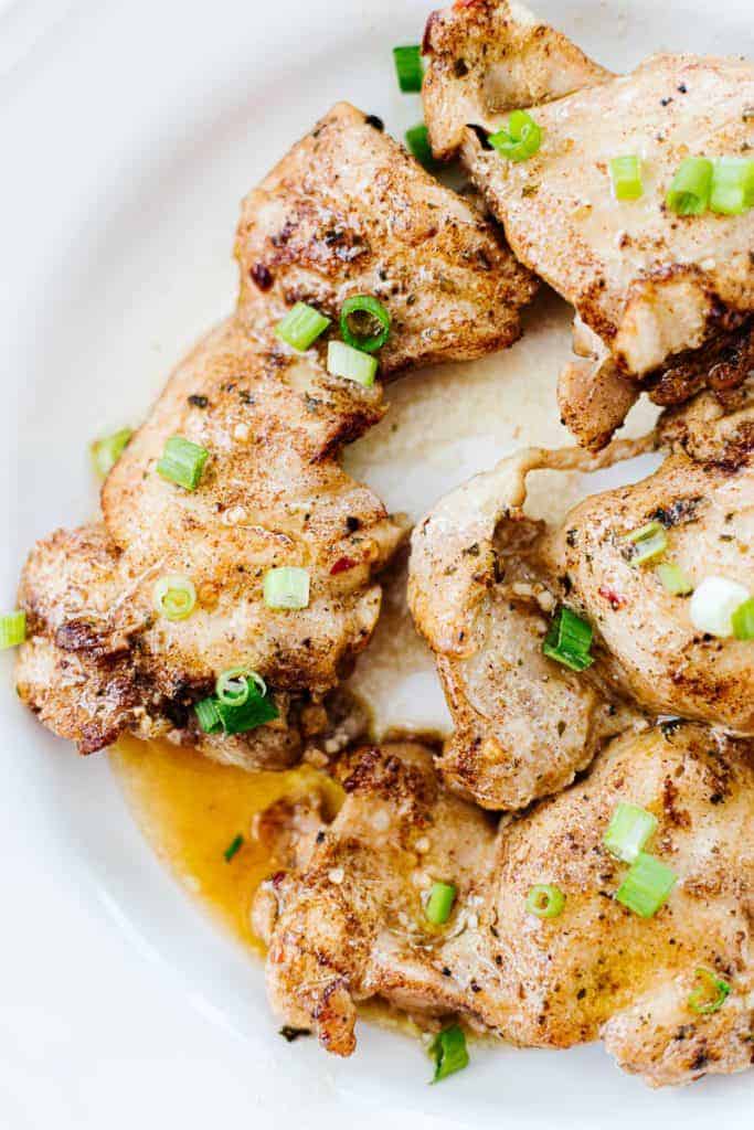 Close up of Instant Pot brown butter garlic chicken thighs in white bowl topped with green onions