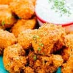 side view of buffalo cauliflower sprinkled with green onions on teal plate next to bowl of sour cream