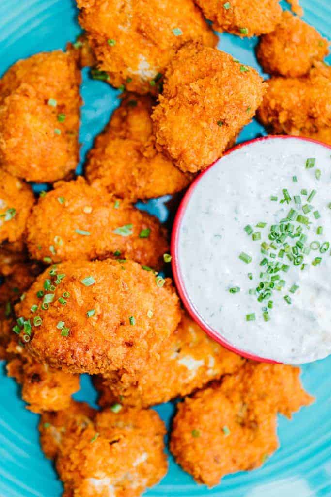 top view of air fryer buffalo cauliflower topped with green onions next to a bowl of sour cream