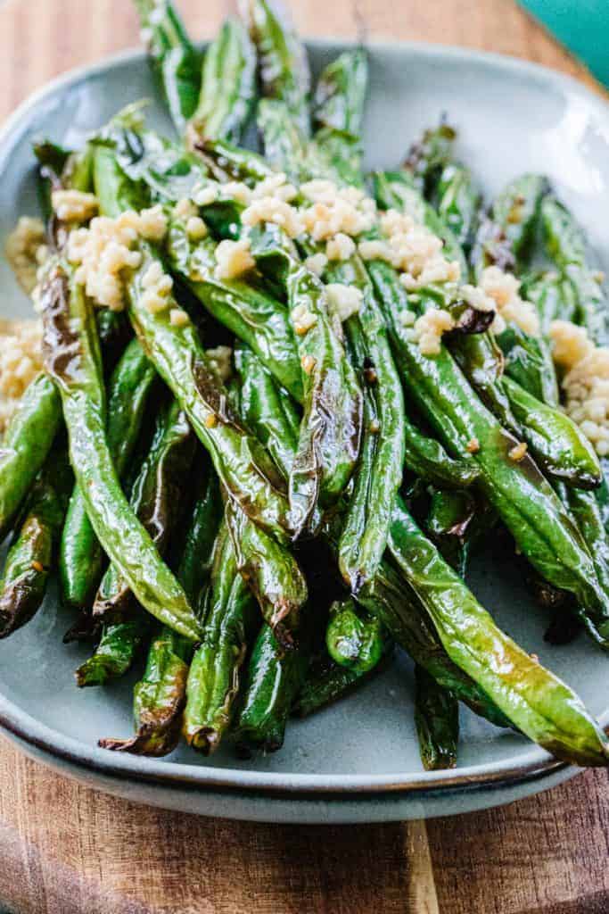 Green beans on a white plate toped with garlic