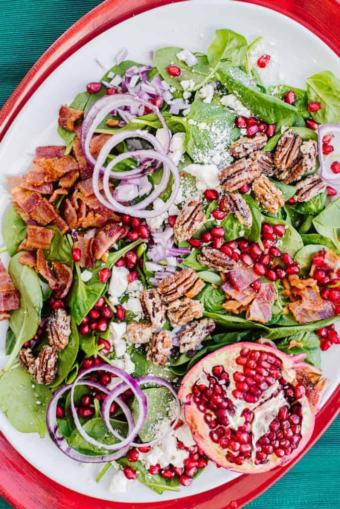 Top view of pomegranate salad with spinach, onion, air fryer bacon, feta cheese, and pecans all on a white and red plate