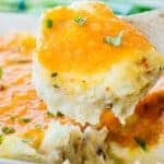 Close up of potato casserole scooped from pan topped with cheese and green onions