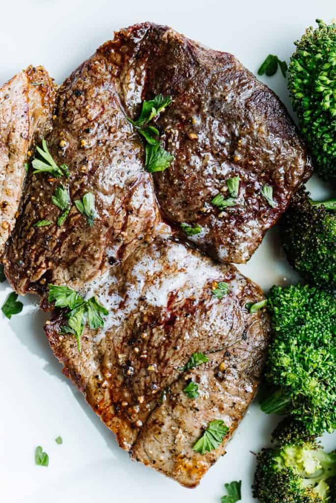 Close up of air fryer steak topped with butter and parsley on a white plate