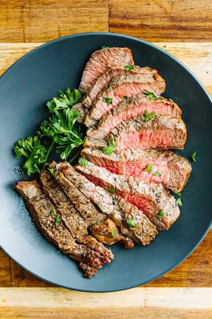 Cut air fryer steak with pink centers next to parsley on a dark plate on a wooden surface