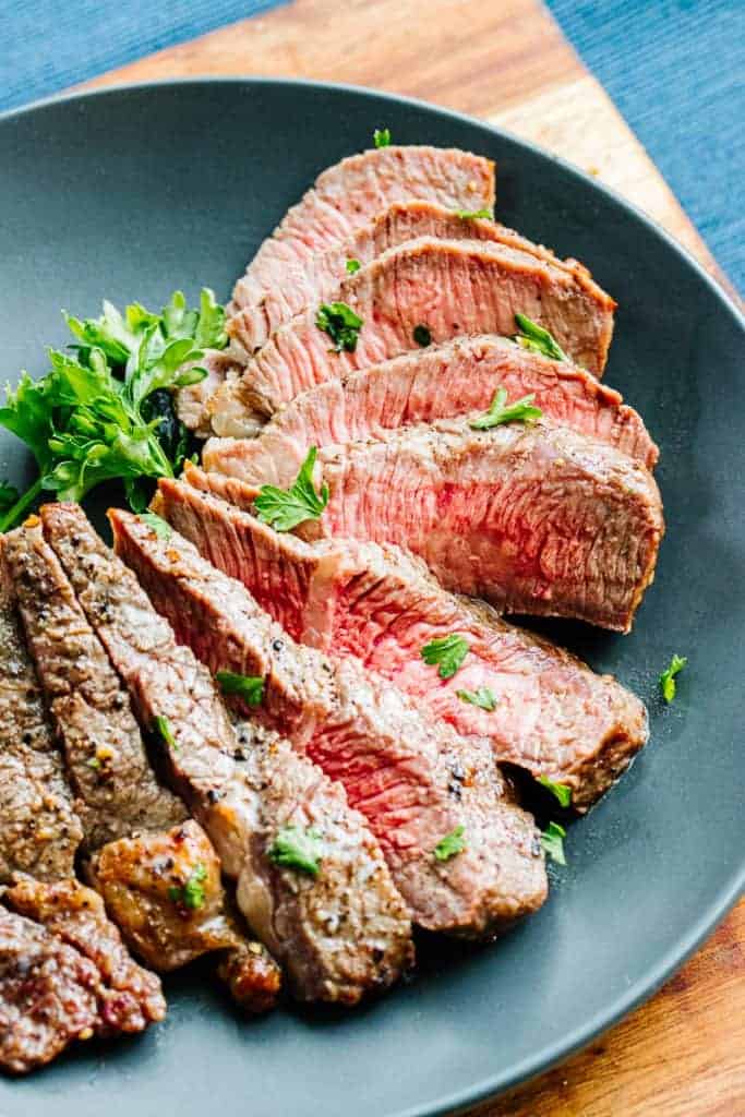 Close up of cut air fryer steak with pink centers next to parsley on a dark plate on a wooden surface