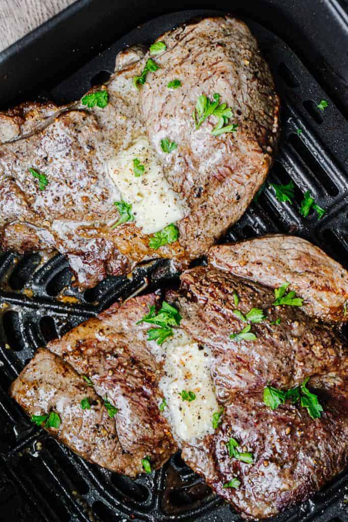 Air Fryer steak in air fryer topped with butter and parsley