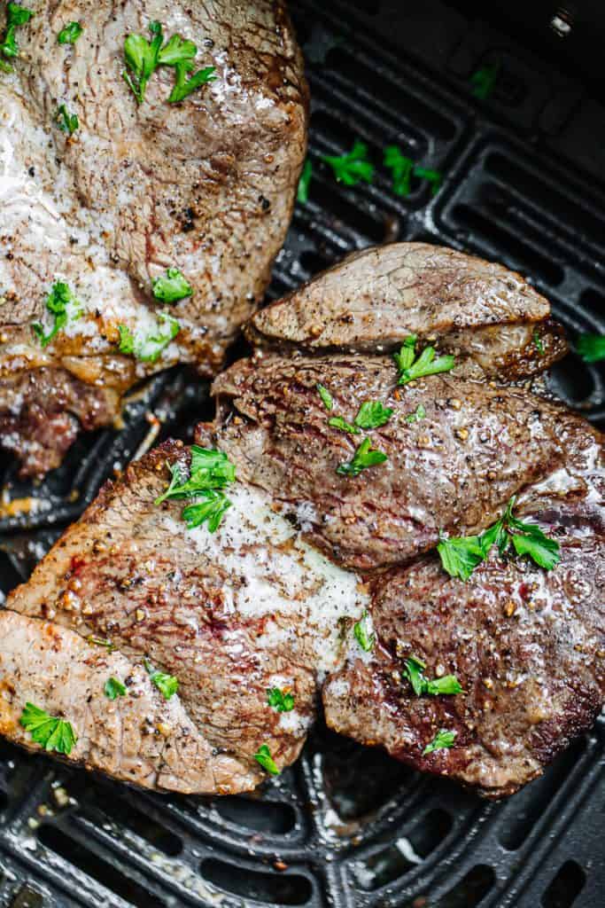 Close up of finished air fryer steak in air fryer topped with butter and parsley