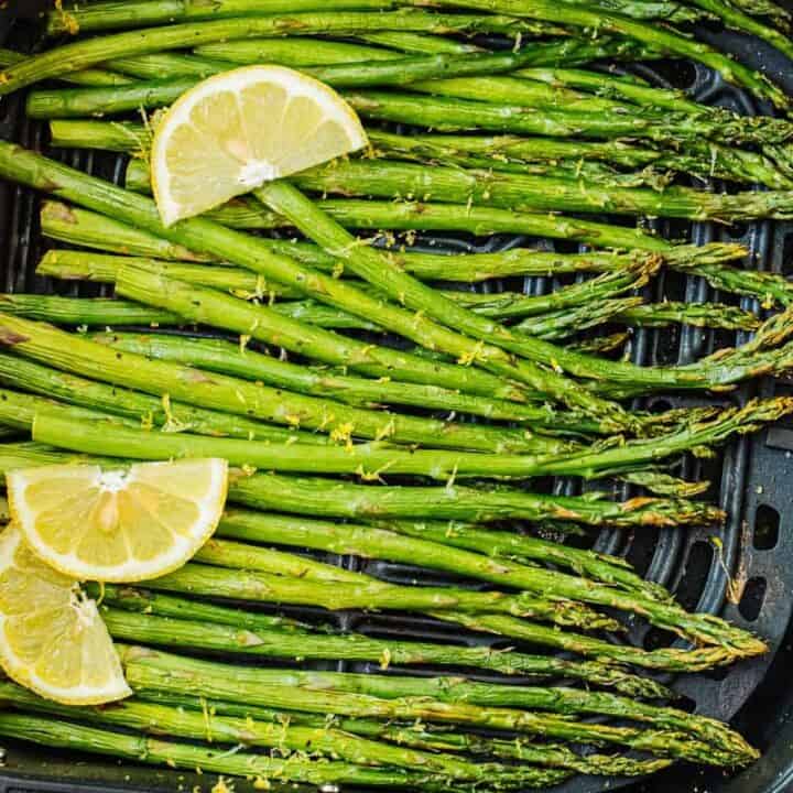 an air fryer basket with asparagus spears and 3 lemon wedges