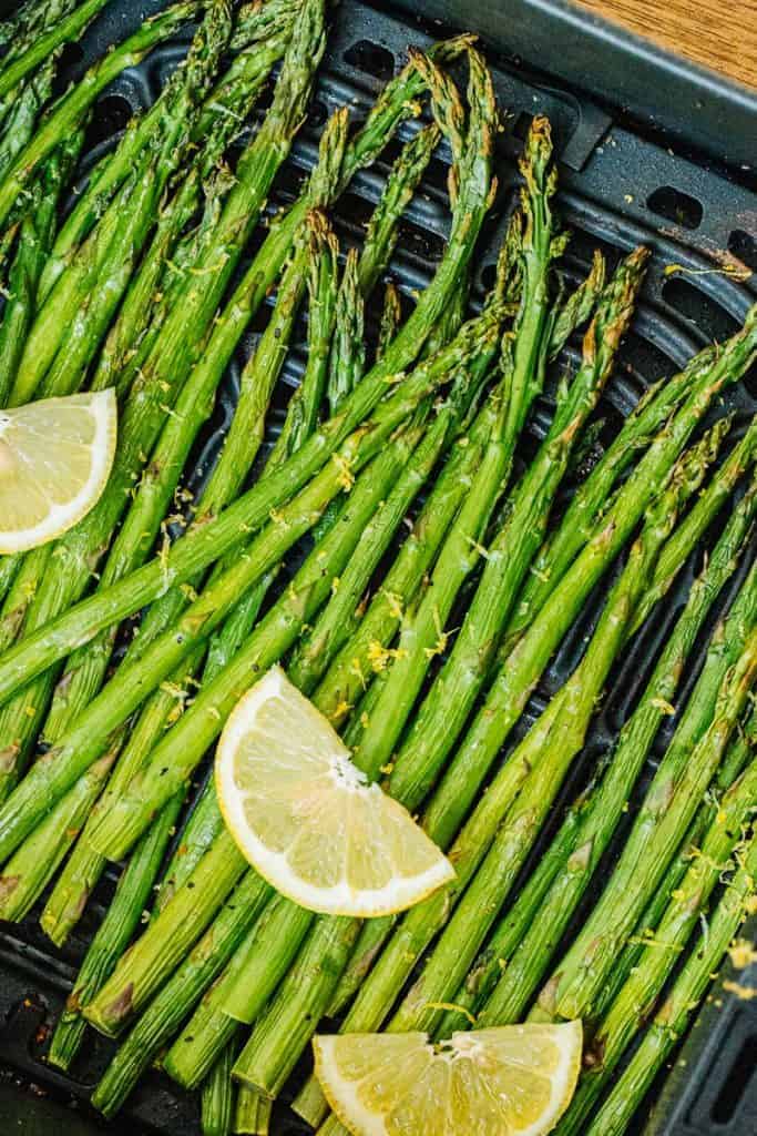 an air fryer basket with asparagus spears and 3 lemon wedges