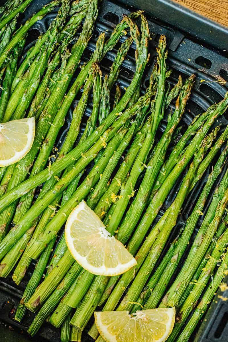 an air fryer basket with asparagus spears and 3 lemon wedges