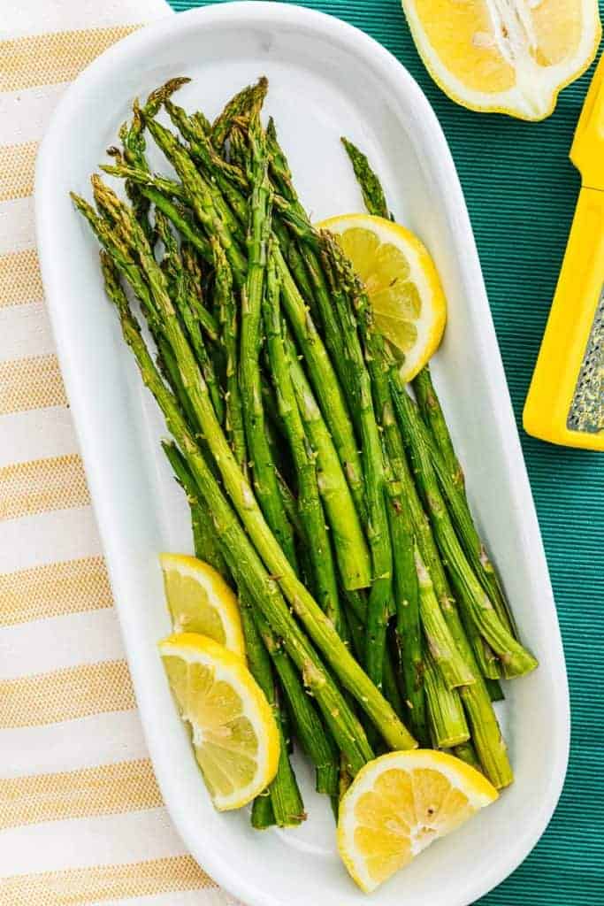 asparagus on a white oblong platter with lemon slices and a yellow striped napkin